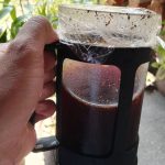 A hand folding a cold brew coffee on a French press container. Best Coffee Beans For Cold Brew Coffee.
