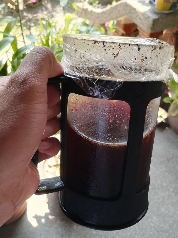 A hand folding a cold brew coffee on a French press container. Best Coffee Beans For Cold Brew Coffee.